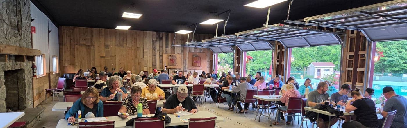 Rows of players marking their bingo cards in a rustic hall with the garage doors open to the trees