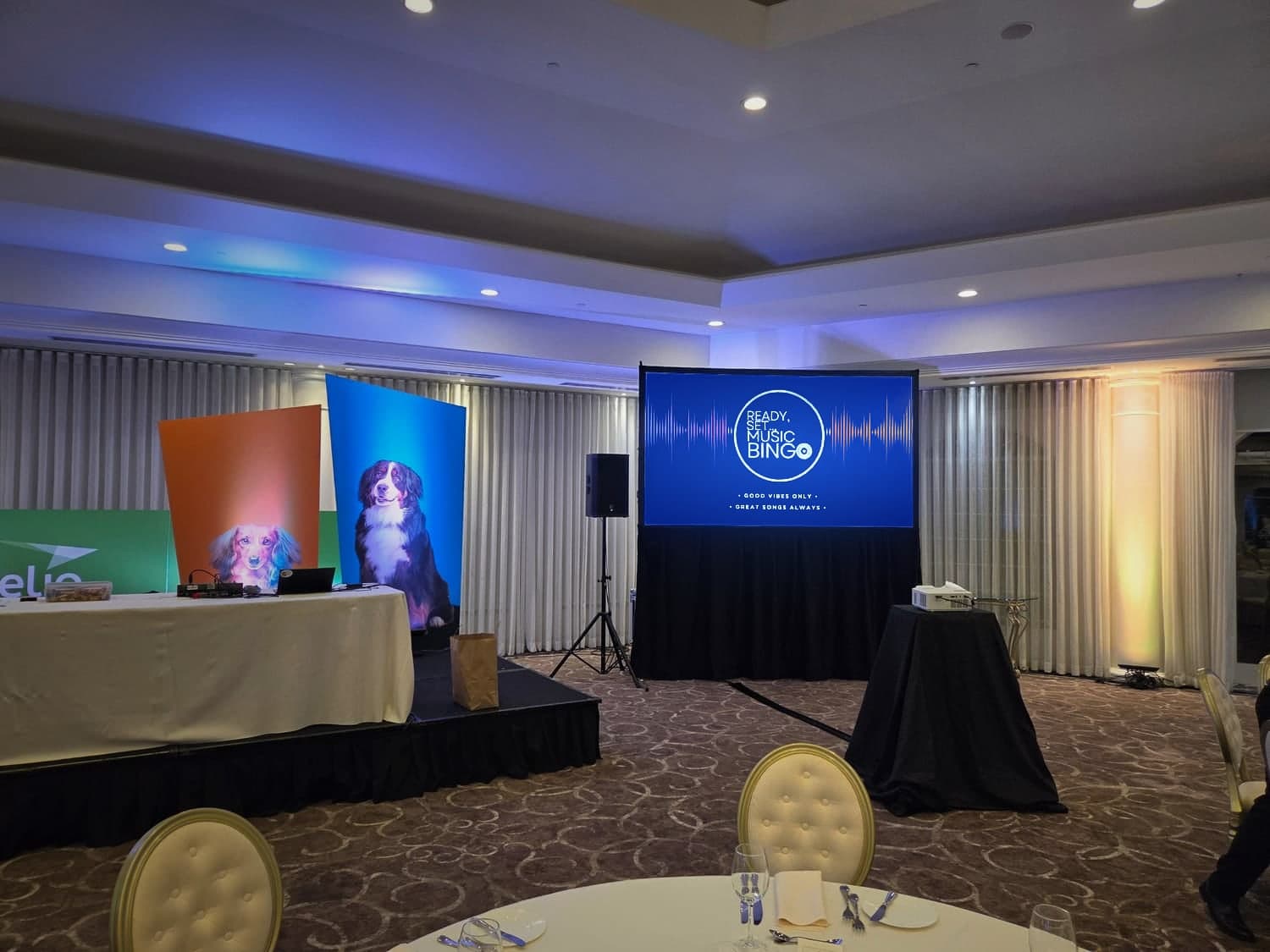 A stage with a Ready Set Music Bingo screen and colourful dog backdrops set up for a corporate event in a hotel ballroom